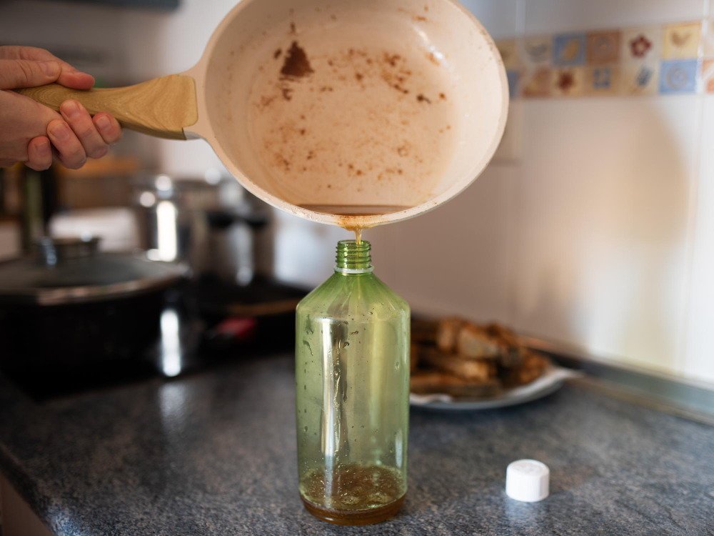 Pessoa despejando óleo de cozinha usado de uma frigideira em uma garrafa plástica sobre a bancada da cozinha.